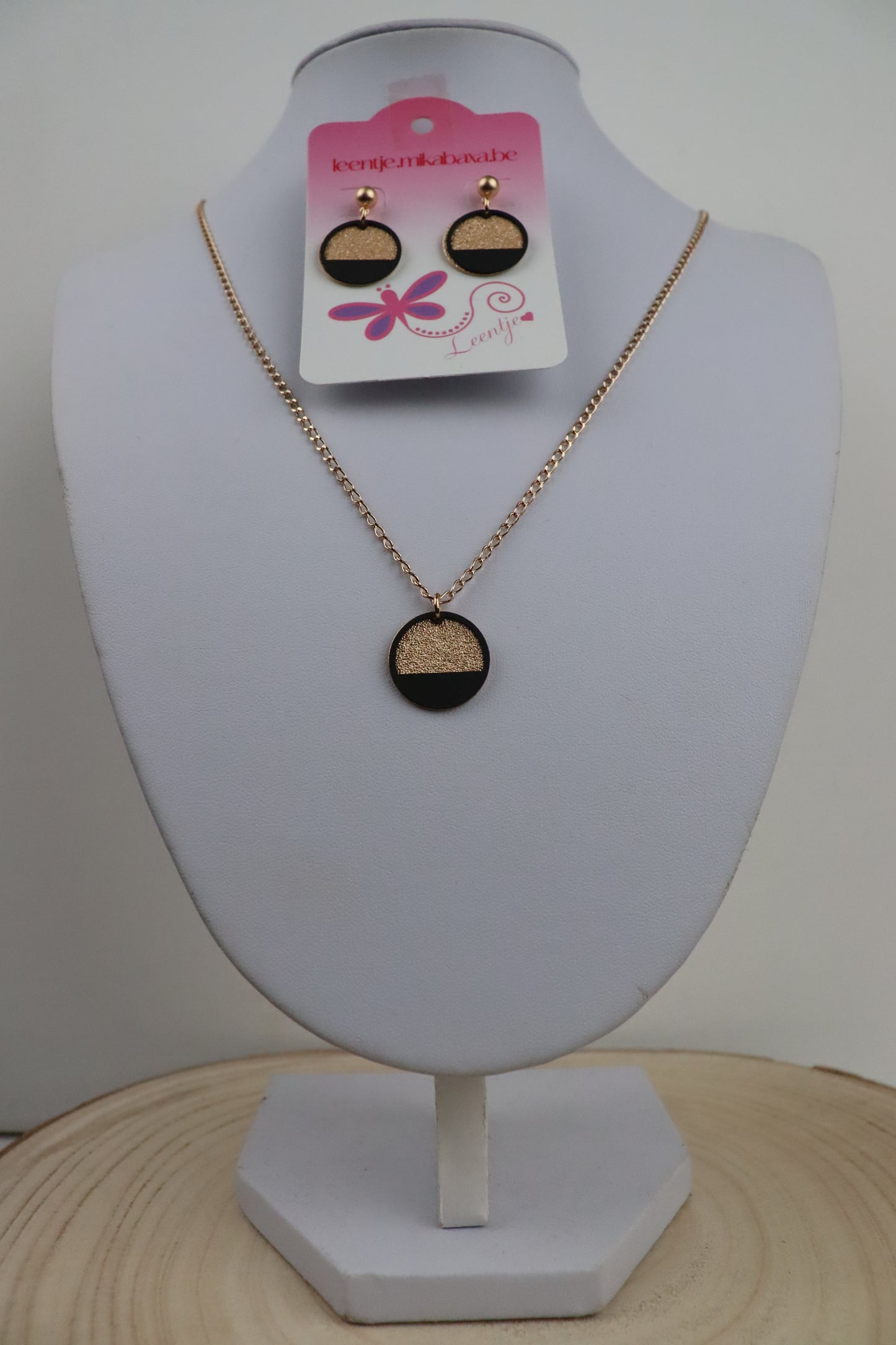 Goudkleurige ketting  met goudkleurige ronde en zwarte halve cirkel  en goudkleurige oorknopjes met goudkleurige ronde en zwarte halve cirkel