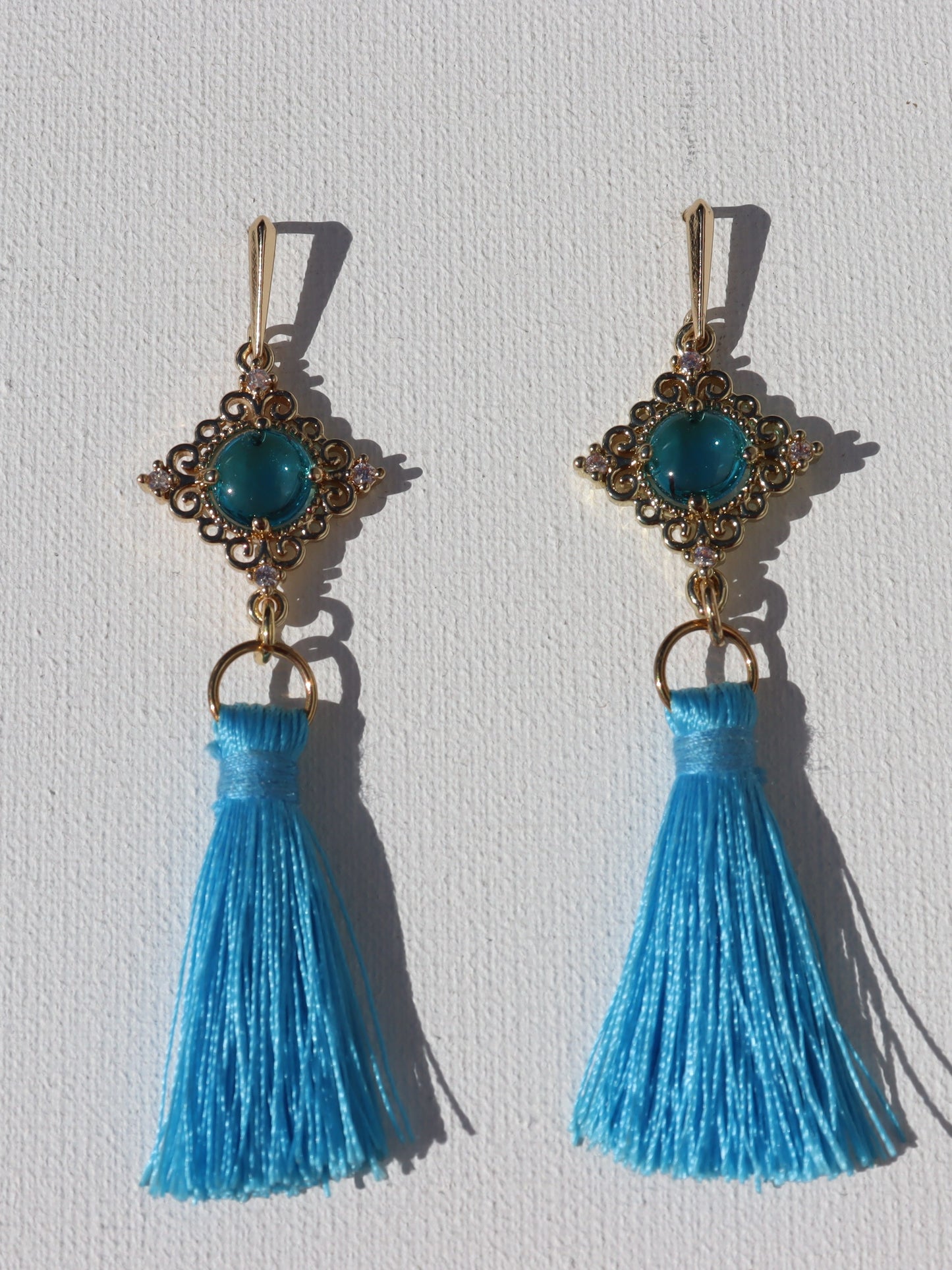 Goudkleurige oorhaken met goudkleurige blauwe steenhanger en blauwe floche