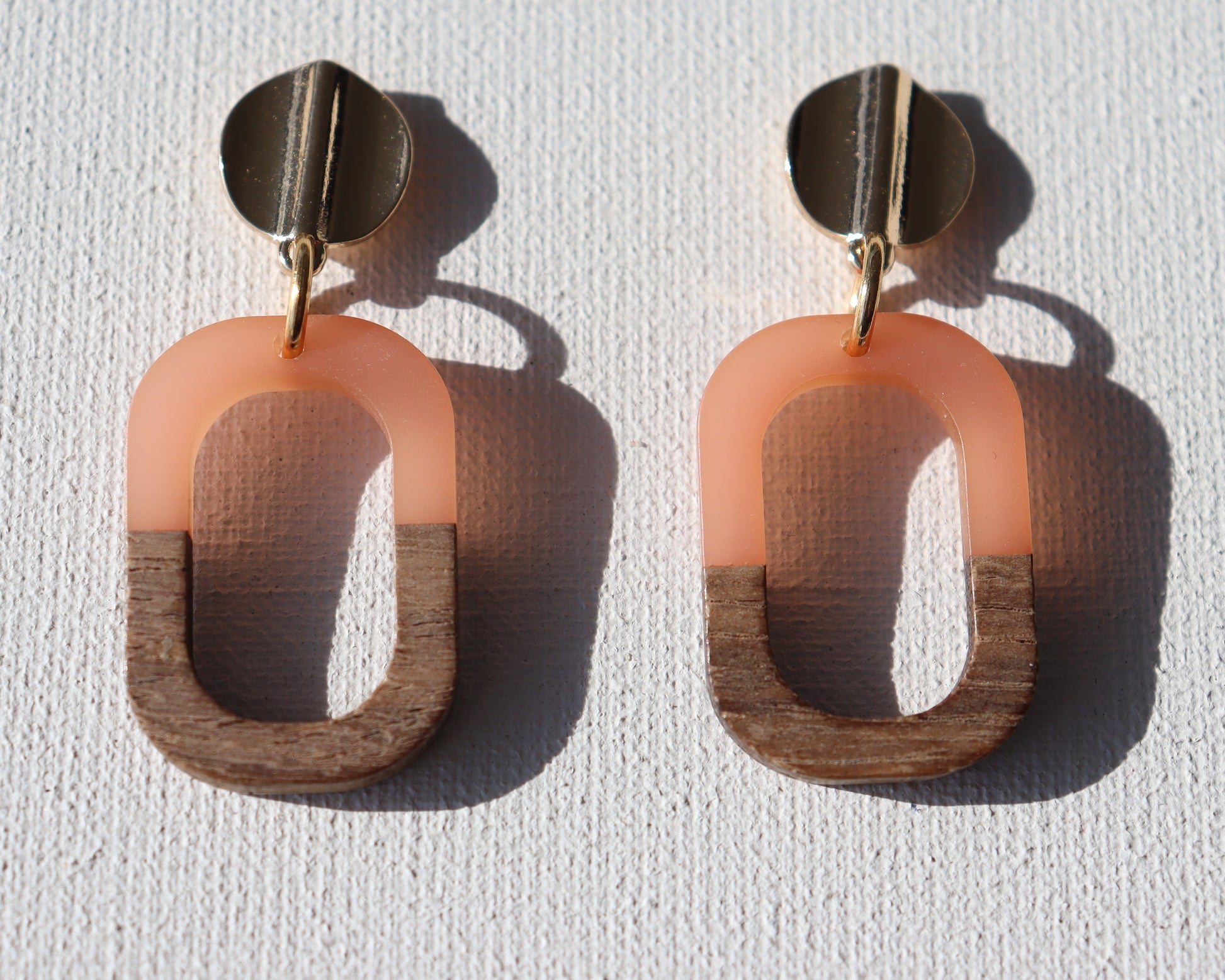 Goudkleurigerondegolfstekertjesmethoutenopenrechthoekmet zalmroze kunsthars