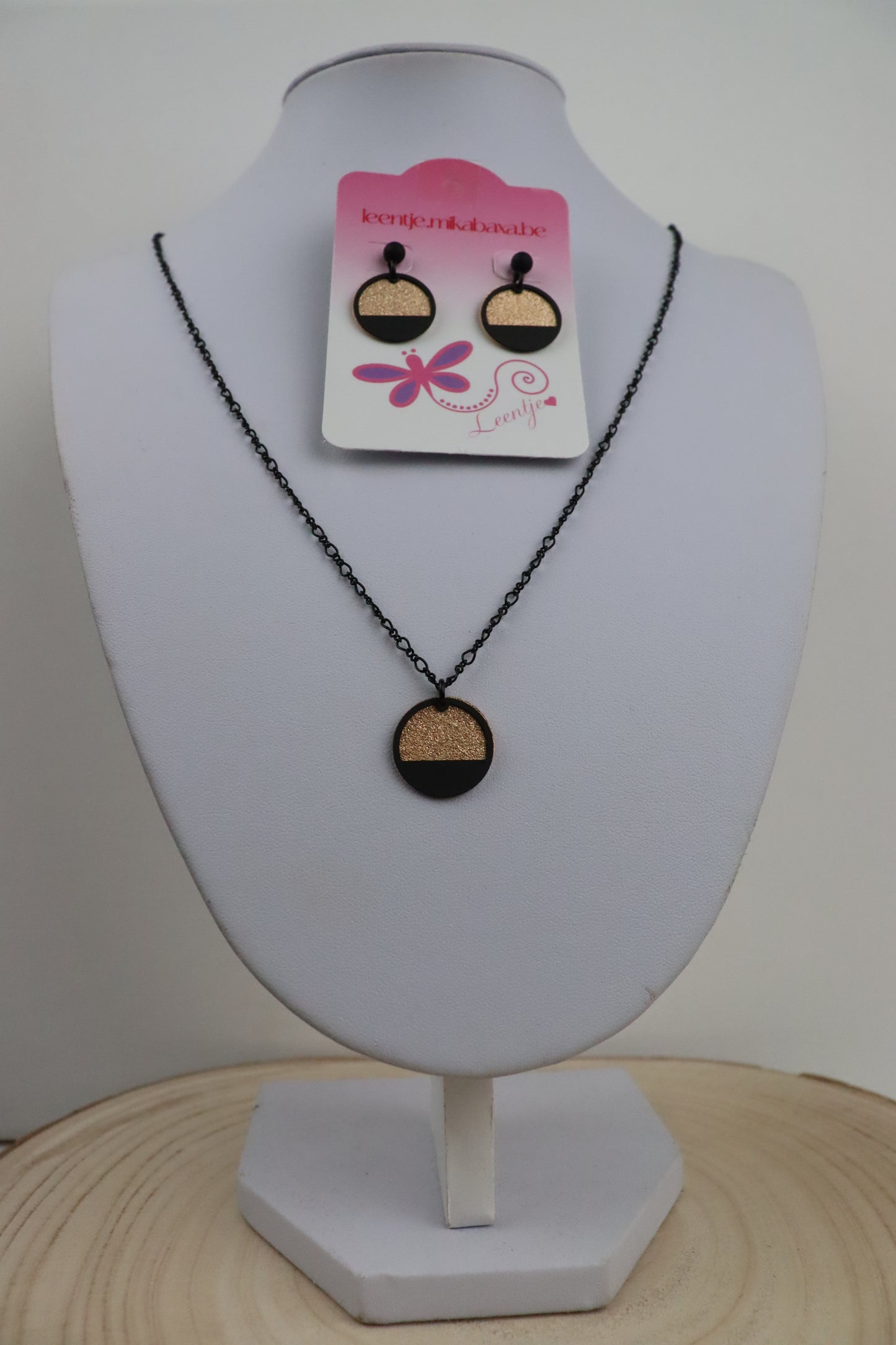 Zwarte_ketting_met_goudkleurige_ronde_en_zwarte_halve_cirkel_en_zwarte_oorknopjes_met_goudkleurige_ronde_en_zwarte_halve_cirkel