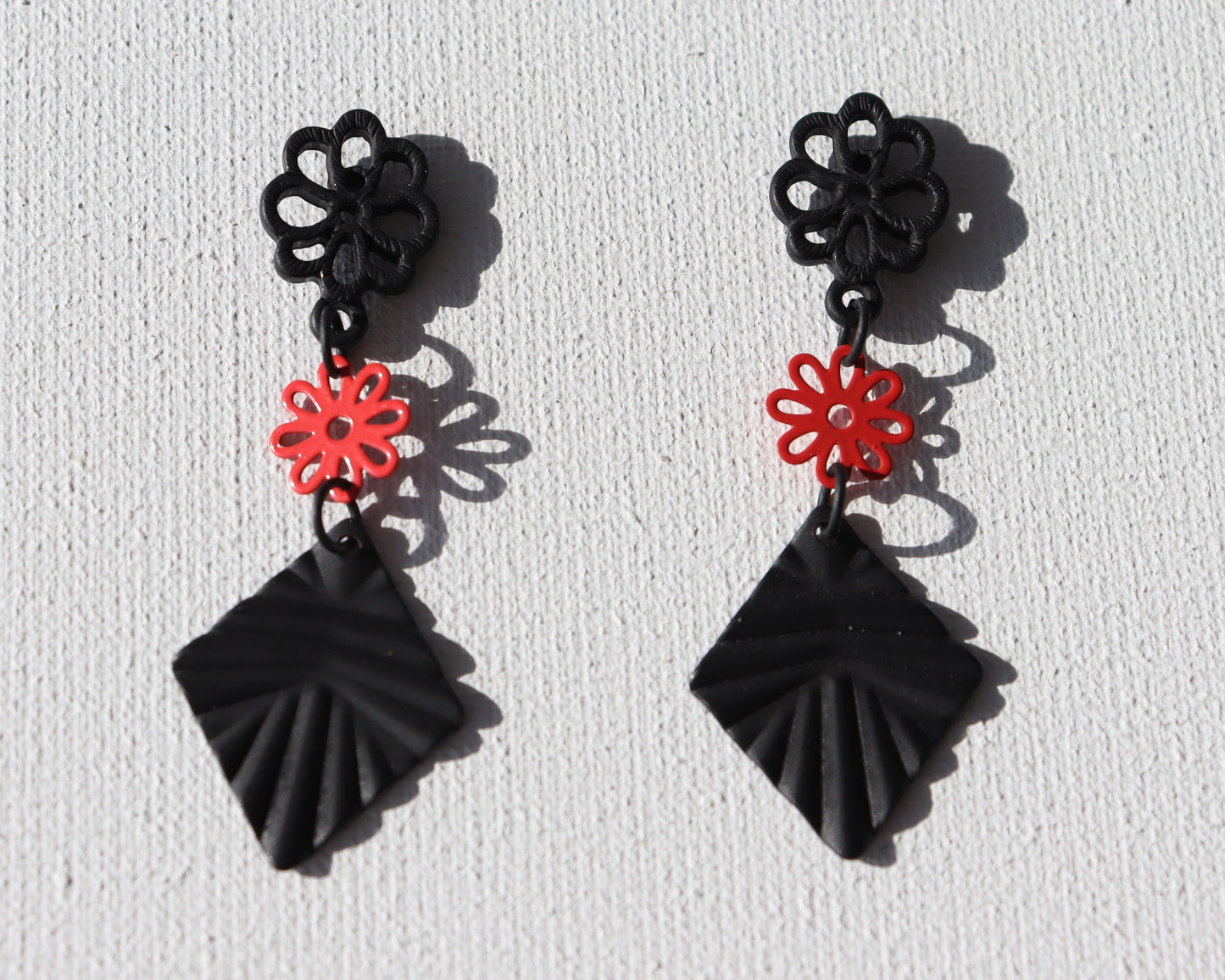 Zwarte bloem oorstekers met rood bloemetje en zwarte geribbelde ruit