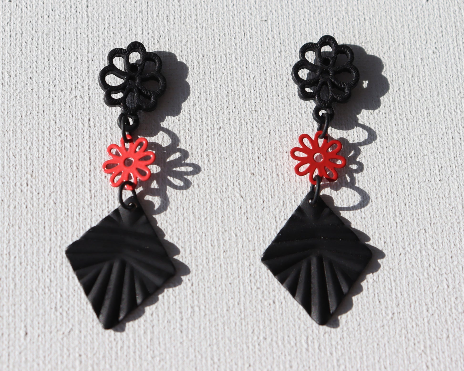 Zwarte bloem oorstekers met rood bloemetje en zwarte geribbelde ruit